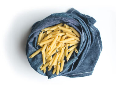foodiesfeed.com pasta penne in blue linen on a white background