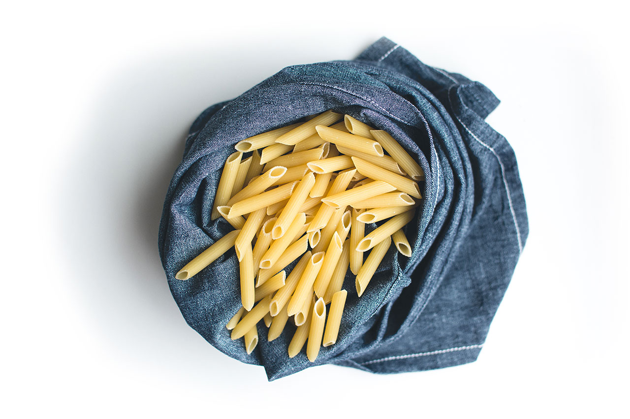 foodiesfeed.com pasta penne in blue linen on a white background